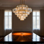 A dramatic geometric brass chandelier centered above a long walnut dining table, acting as the visual anchor of the room and defining the gathering space.