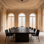 A luxurious and spacious dining room showcasing a large, solid reclaimed oak dining table perfectly proportioned to the high ceilings and architectural volume of the room, creating inherent balance and visual harmony. Soft natural light illuminates the elegant space with sleek, minimalist chairs.