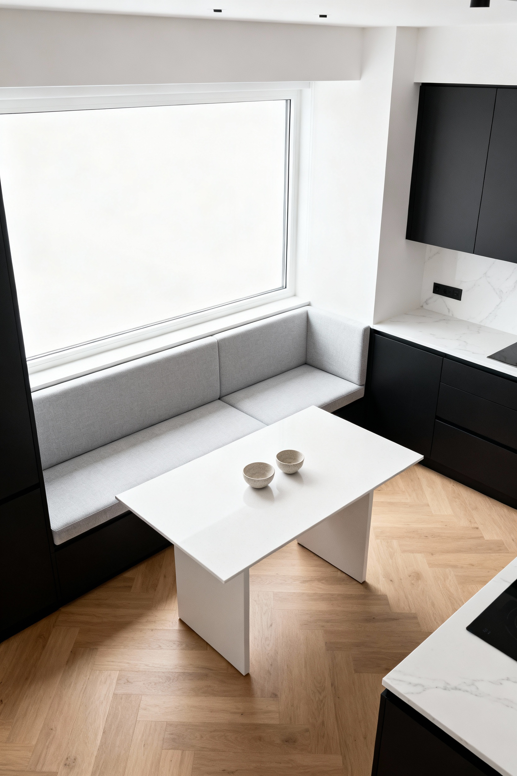 Modern kitchen corner featuring a built-in L-shaped light gray banquette bench and a minimalist white dining table, showcasing a space-saving integrated dining solution.