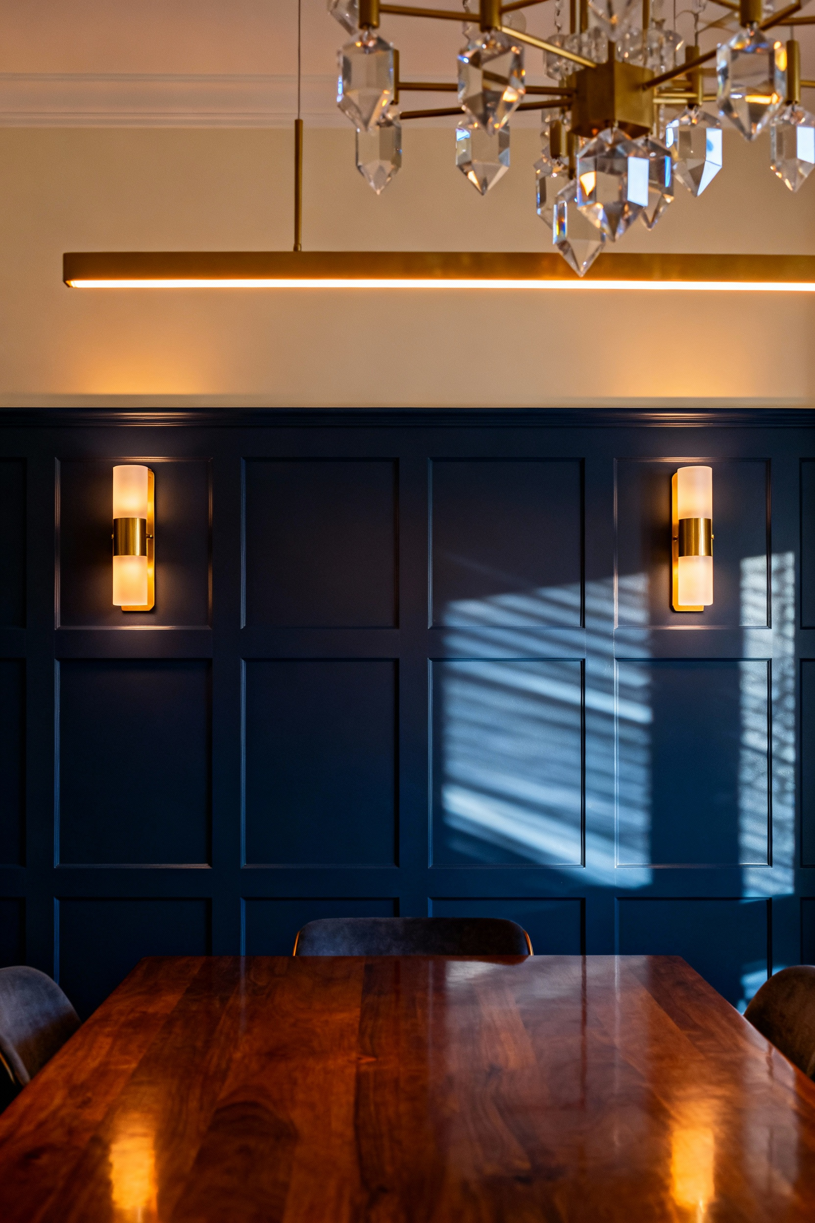 Interior view of a luxurious dining room showing the warm, layered glow created by two strategically placed wall sconces and a central chandelier, highlighting architectural depth.