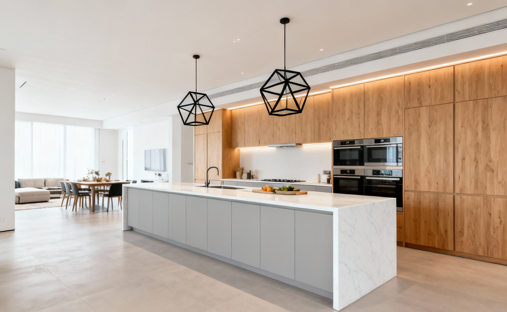 A wide view of a minimalist open-concept modern kitchen featuring a large white quartz island, light gray handleless cabinets, and light oak wood storage, designed to accommodate multiple users and collaboration.