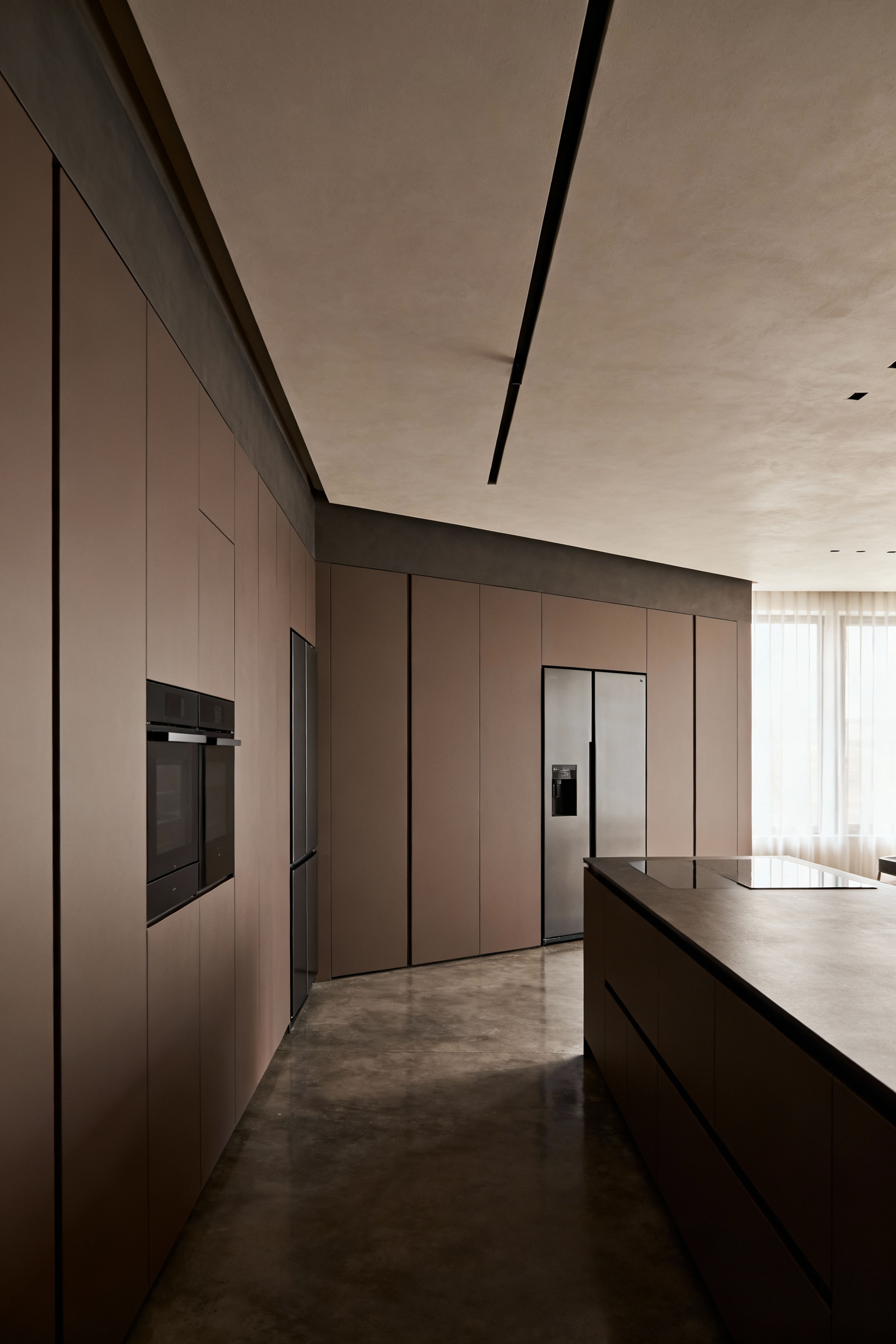 A modern, minimalist kitchen featuring seamless, handleless, matte taupe floor-to-ceiling cabinets that form an unbroken architectural wall, maximizing vertical storage and enhancing the room's perceived height.