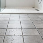 A modern curbless shower floor made of small, matte grey porcelain tiles with visible textured surface and contrasting grout lines, designed for high slip resistance and universal accessibility.