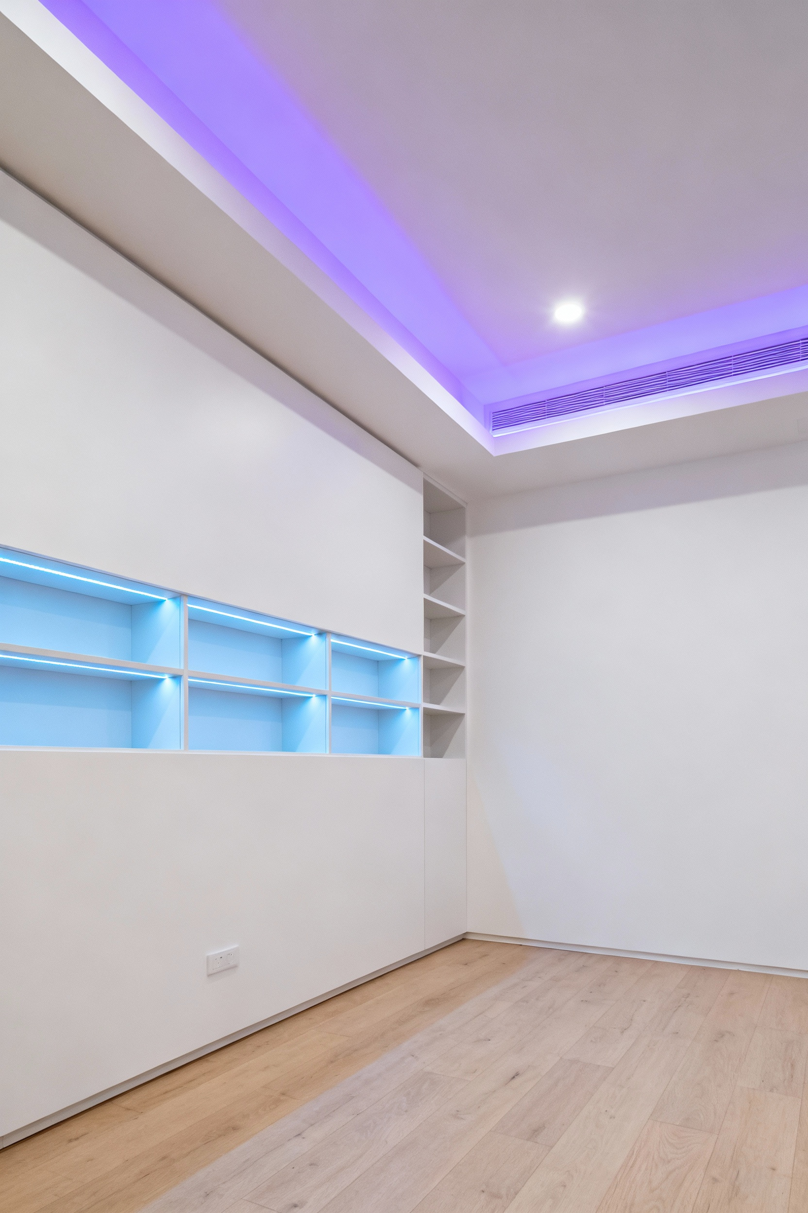 Modern kid's bedroom with seamless tech integration, showing built-in wall niches and a false ceiling illuminated by soft, sapphire blue and lavender indirect LED smart lighting.