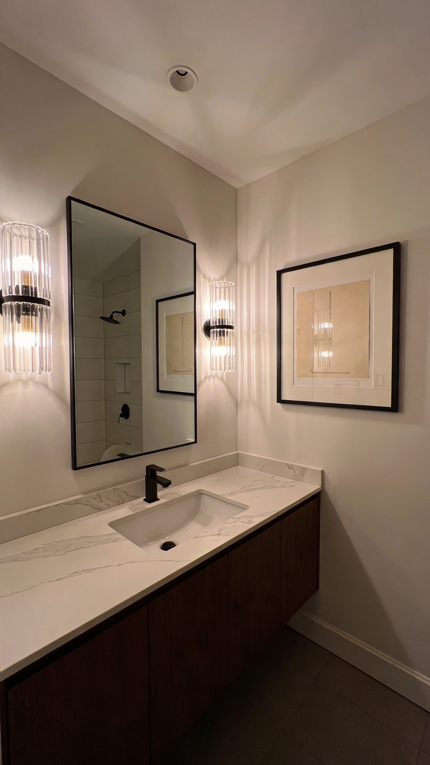High-end bathroom interior showing vanity sconces illuminating a framed art piece on the side wall with side-grazing light.