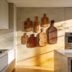 A bright open-concept kitchen featuring a display of rustic wooden breadboards on the wall to add warmth to the modern stone and cabinet surfaces.