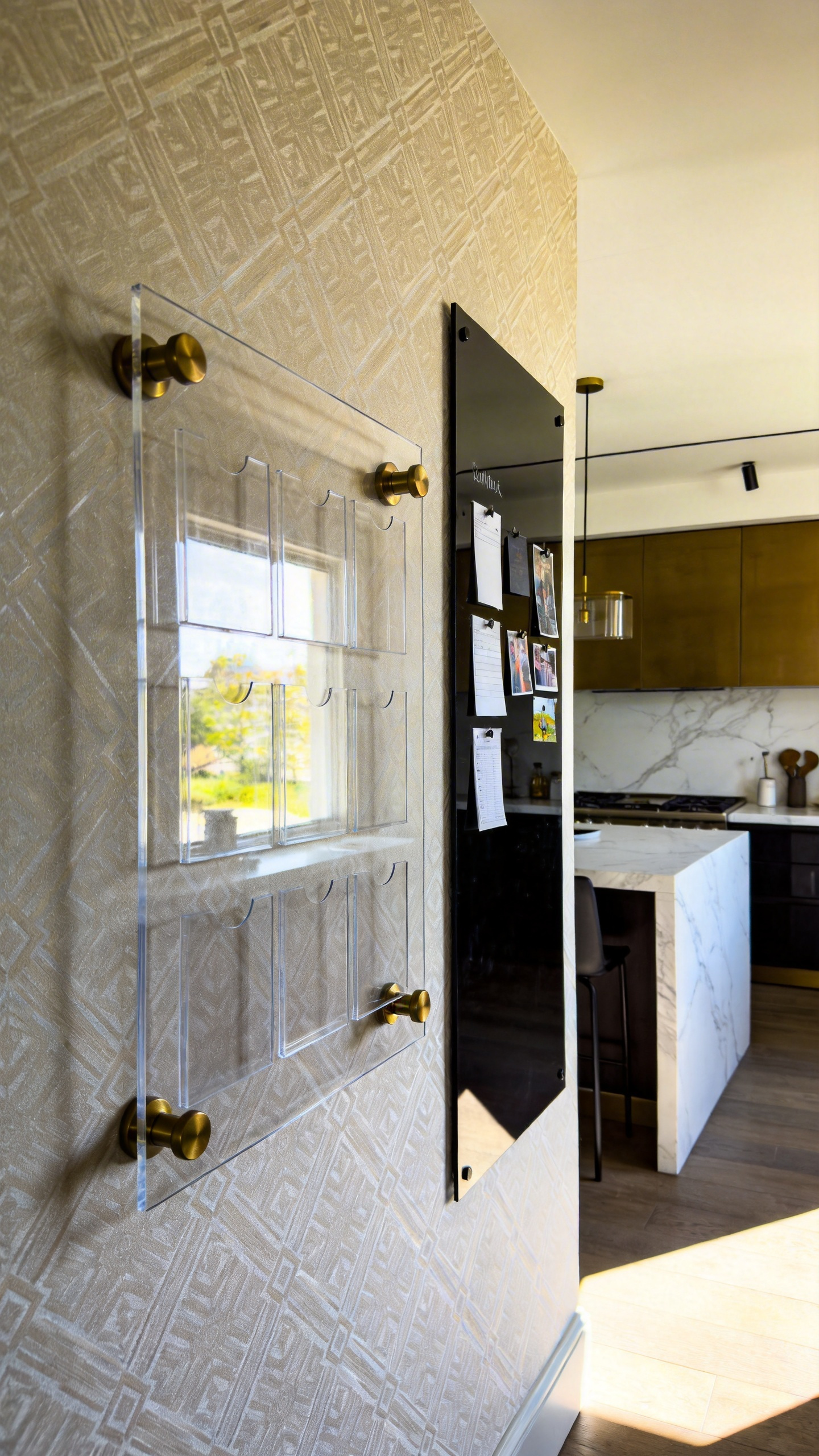 A modern kitchen wall decor command center featuring a floating acrylic calendar with brushed brass hardware against stylish wallpaper.