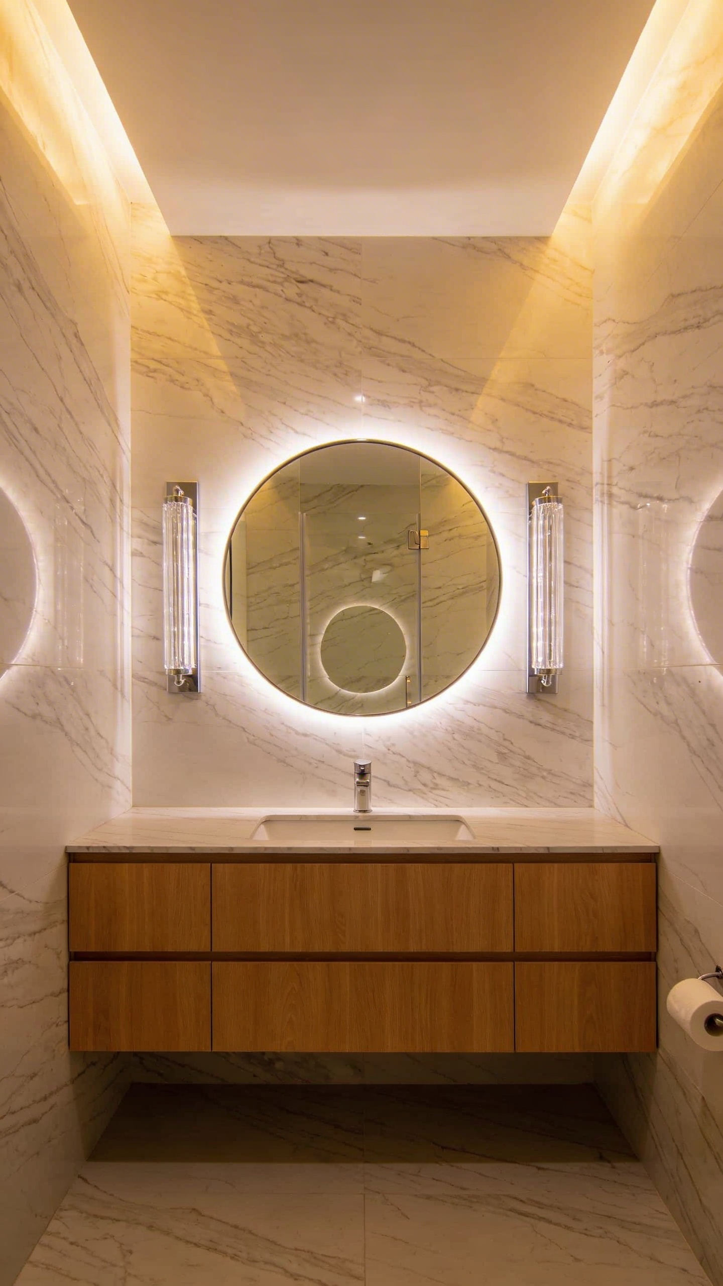 A small modern bathroom with layered lighting including eye-level vertical sconces and a backlit mirror to remove dark shadows.
